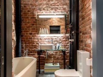 Pareti di mattoni, impianti idraulici bianchi e mobili di vetro in un bagno in stile loft