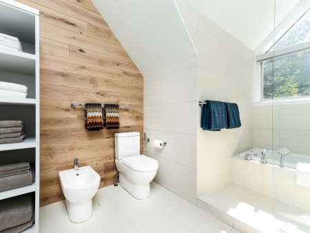 Salle de bains scandinave - murs en bois véritable, baignoire blanche, plafond blanc, serviettes avec des motifs scandinaves nationaux.