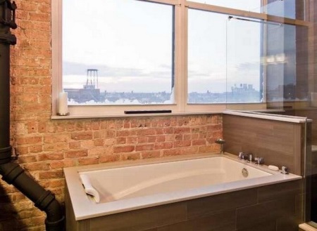 Bagno nel loft con muri di mattoni, grandi finestre e linee di utilità senza ostacoli