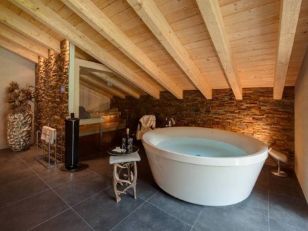 Badrum i stugan - med trätak, stort badkar, stenväggar och -golv.